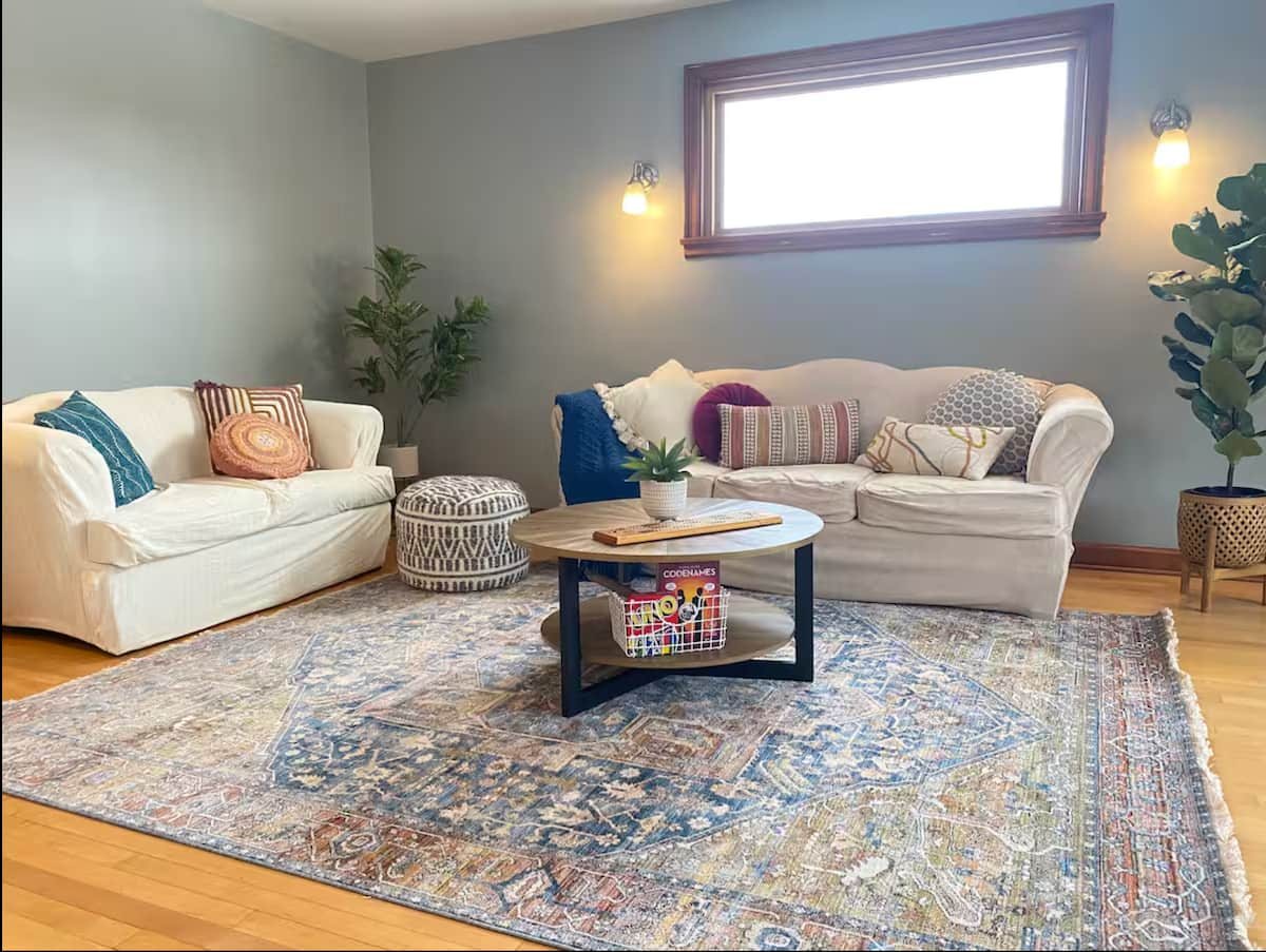 Bright living room with two sofas, a patterned rug, and upper-floor windows
