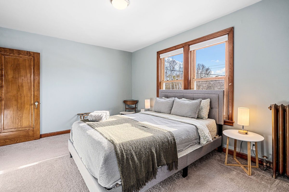 Bedroom 1 with a gray queen bed, two windows, bedside lamps, and original woodwork