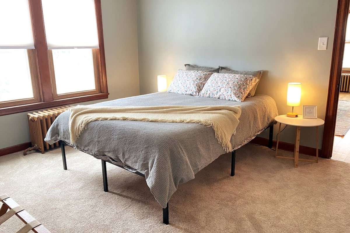 Bedroom 2 with a gray queen bed, floral pillows, two windows, and bedside lighting