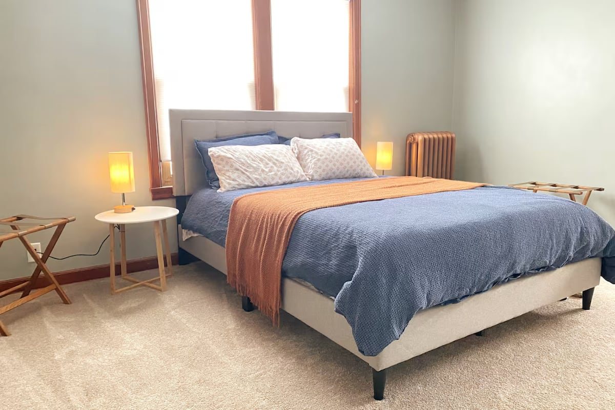 Bedroom 3 with a blue queen bed, rust-colored throw, bedside lamps, and luggage racks