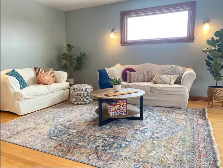 Bright living room with two sofas, a patterned rug, and upper-floor windows